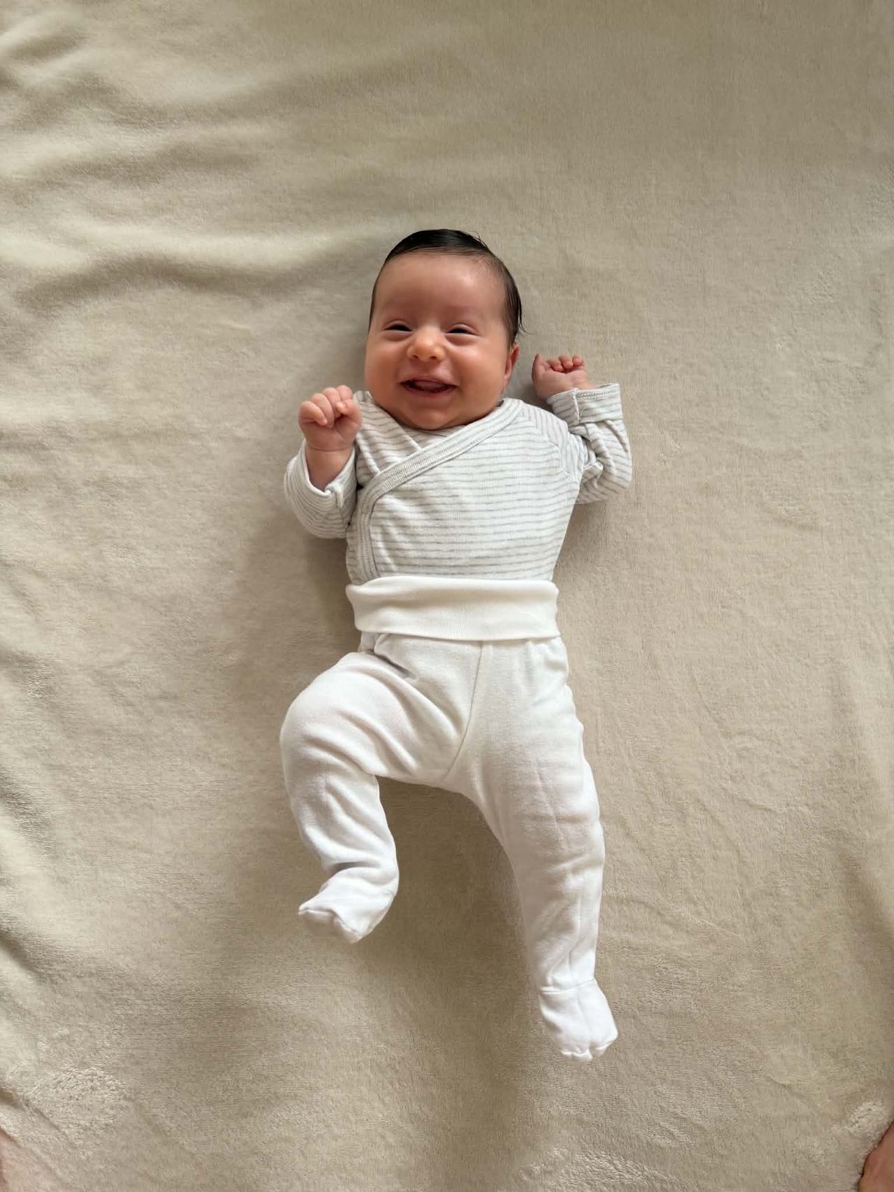 Sofia, nyfödd, ligger på en ljus filt och ler stort mot kameran.